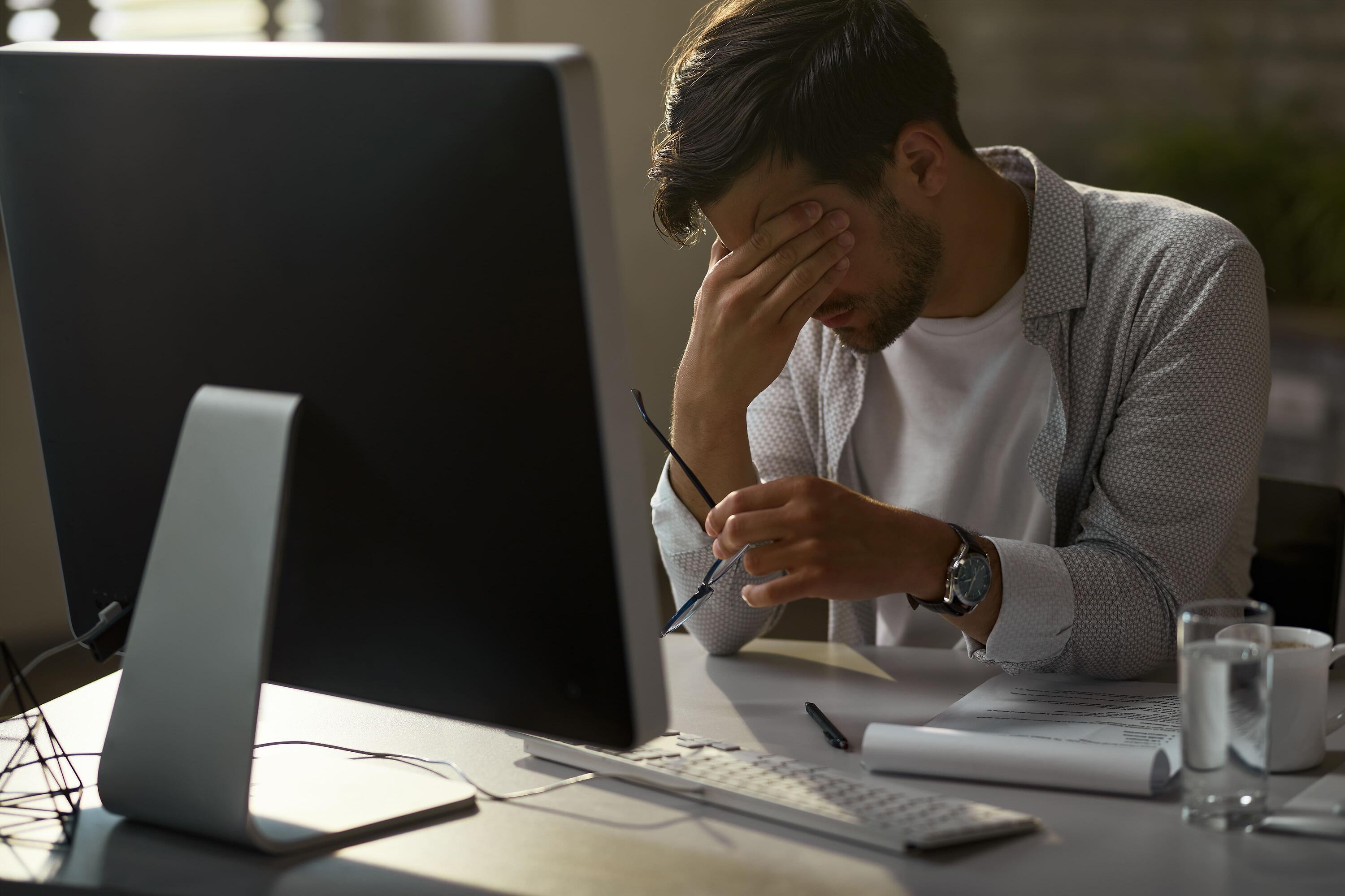 exhausted-businessman-holding-his-head-pain-while-working-desktop-pc-office
